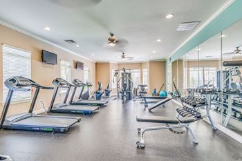 a fitness room with cardio equipment and windows